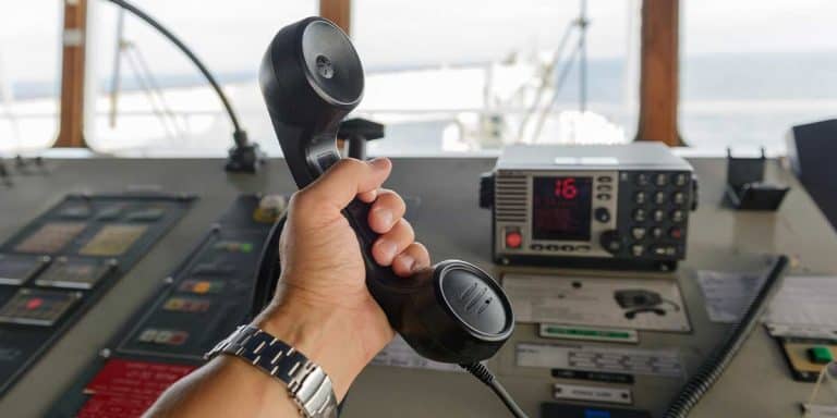 VHF handset in a sailor's hand with the base station in the background