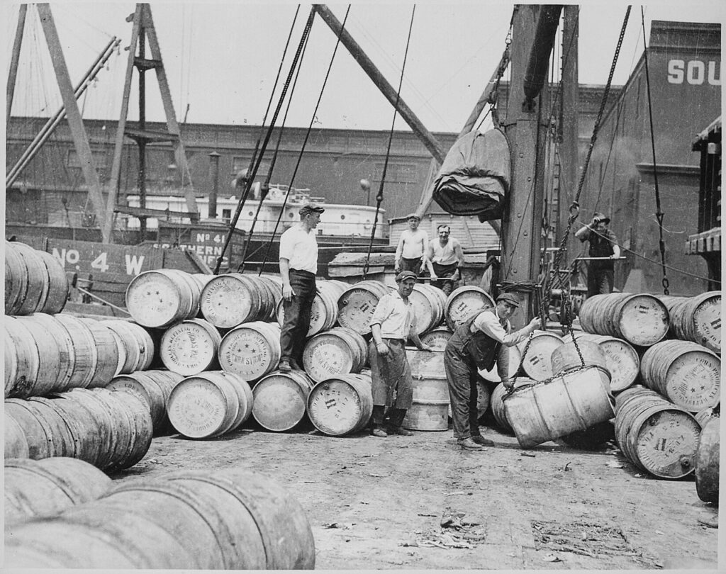 A black and white photograph showing stevedores loading barrels onto a ship